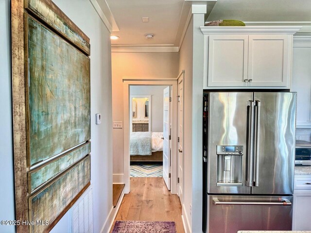 hall featuring baseboards, crown molding, and light wood finished floors