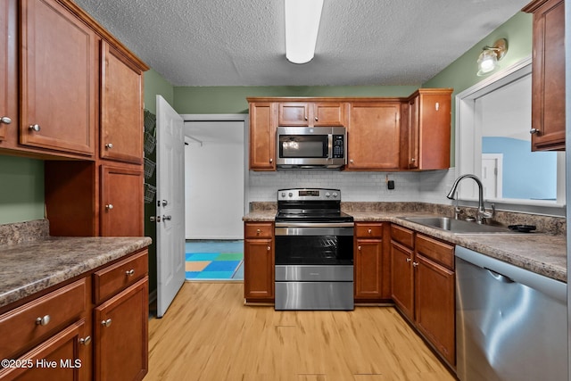 kitchen featuring light wood finished floors, brown cabinets, stainless steel appliances, tasteful backsplash, and a sink