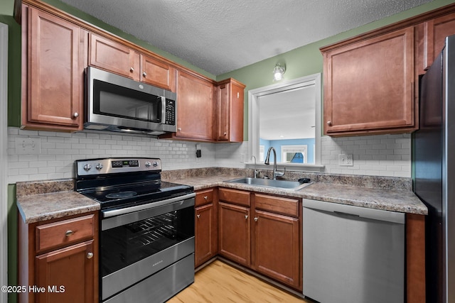 kitchen with a sink, tasteful backsplash, appliances with stainless steel finishes, light wood-type flooring, and brown cabinetry