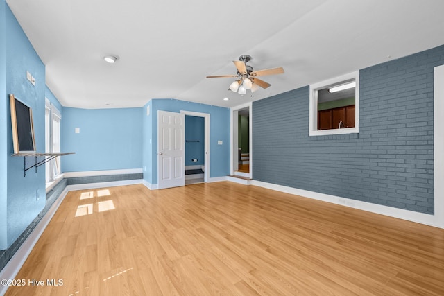 unfurnished living room with light wood-style flooring, baseboards, ceiling fan, brick wall, and an accent wall