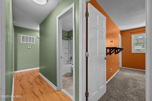 hall featuring a textured ceiling, baseboards, and visible vents