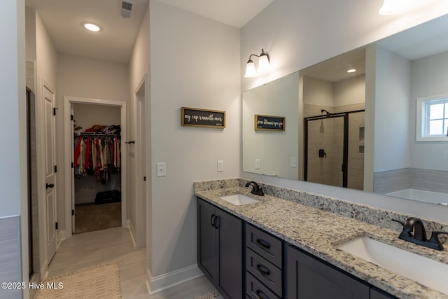 bathroom featuring visible vents, a sink, a stall shower, and a walk in closet