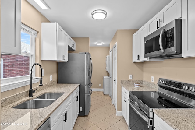 kitchen featuring washer / clothes dryer, appliances with stainless steel finishes, a sink, light tile patterned floors, and white cabinetry