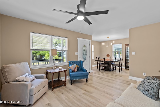 living area with baseboards, plenty of natural light, light wood finished floors, and ceiling fan with notable chandelier