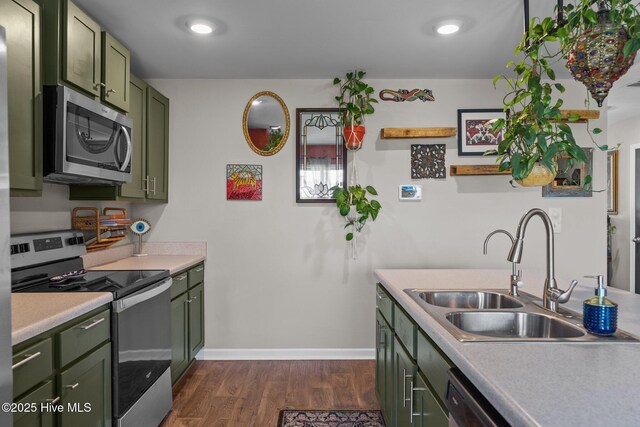 kitchen featuring light countertops, dark wood-type flooring, appliances with stainless steel finishes, green cabinetry, and a sink