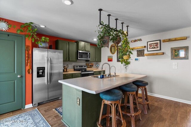 kitchen with a sink, appliances with stainless steel finishes, a kitchen bar, dark wood finished floors, and green cabinets