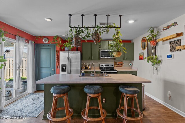 kitchen featuring green cabinets, appliances with stainless steel finishes, a kitchen bar, and a sink