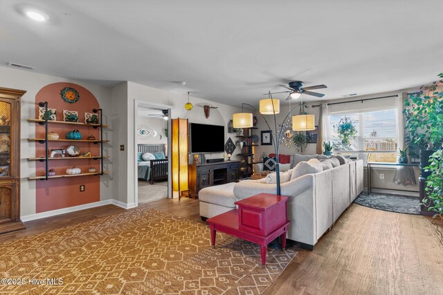 living room with a fireplace, visible vents, a ceiling fan, and wood finished floors