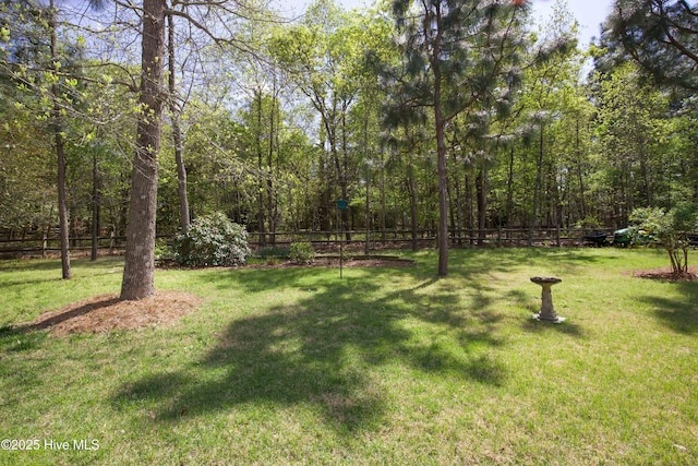 view of yard featuring a wooded view and fence