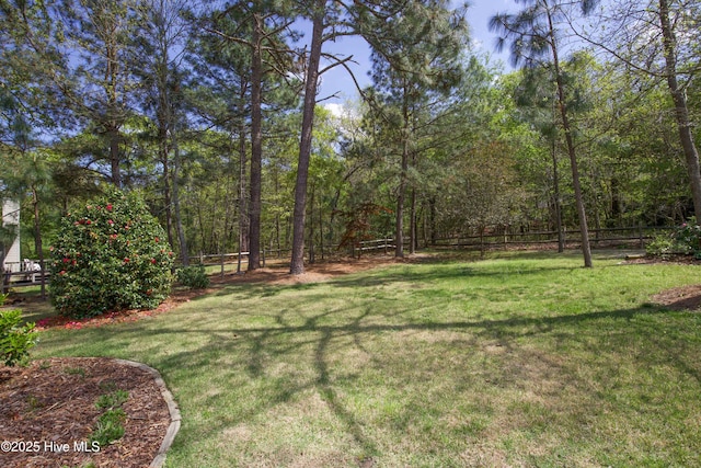 view of yard featuring a wooded view and fence