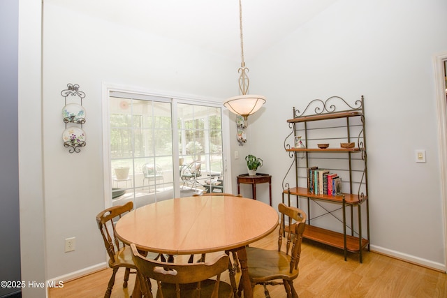 dining space featuring light wood-style flooring, baseboards, and vaulted ceiling