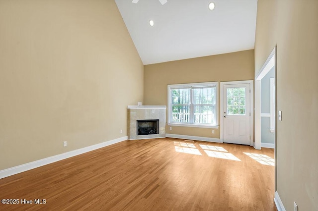 unfurnished living room featuring high vaulted ceiling, light wood-type flooring, baseboards, a tiled fireplace, and recessed lighting