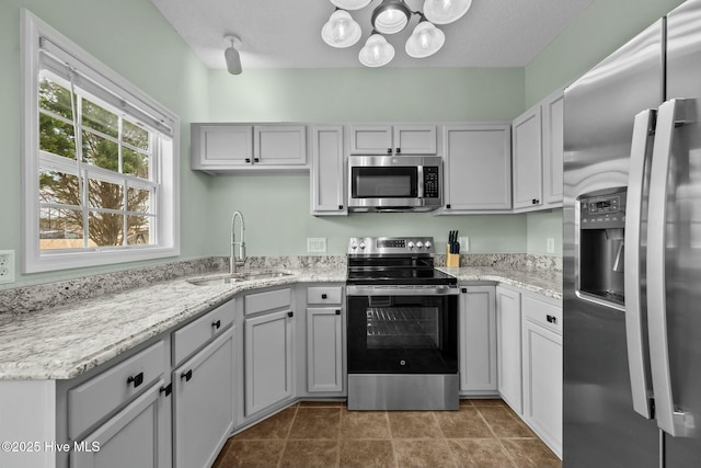 kitchen featuring tile patterned flooring, stainless steel appliances, a sink, light stone counters, and a notable chandelier