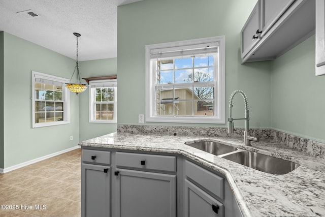 kitchen featuring a textured ceiling, visible vents, hanging light fixtures, a sink, and gray cabinetry