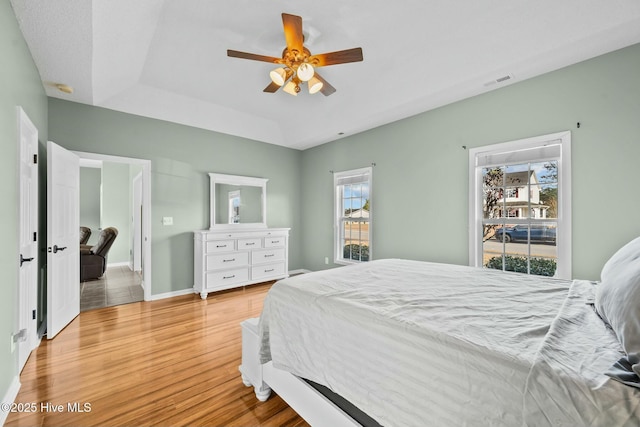 bedroom featuring a ceiling fan, visible vents, baseboards, and wood finished floors