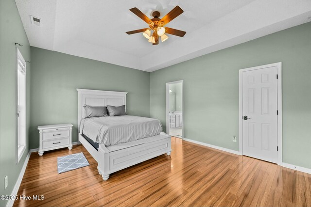 bedroom with wood finished floors, ensuite bath, baseboards, visible vents, and ceiling fan