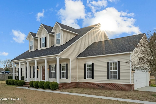 new england style home with a shingled roof, covered porch, and an attached garage