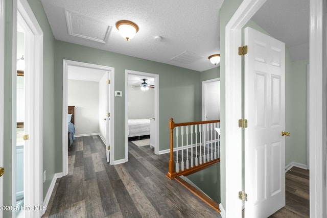 hall with attic access, dark wood-style floors, an upstairs landing, and a textured ceiling
