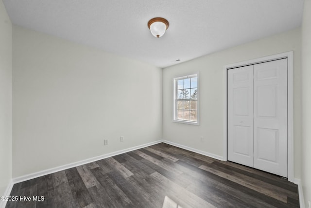 unfurnished bedroom with baseboards, a closet, and dark wood-type flooring