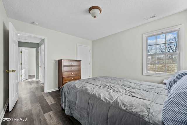 bedroom featuring dark wood finished floors, a textured ceiling, baseboards, and visible vents