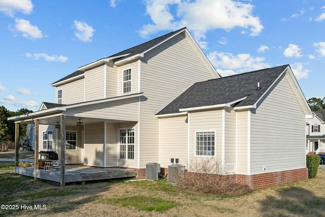 back of property with roof with shingles, central air condition unit, and a yard