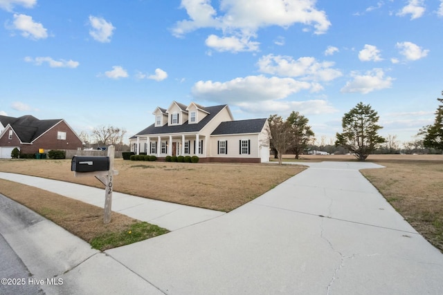 new england style home with a front yard, a porch, and concrete driveway