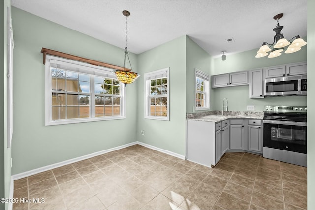 kitchen with a sink, gray cabinetry, stainless steel appliances, baseboards, and an inviting chandelier