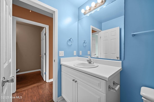 half bathroom featuring vanity, baseboards, toilet, and wood finished floors