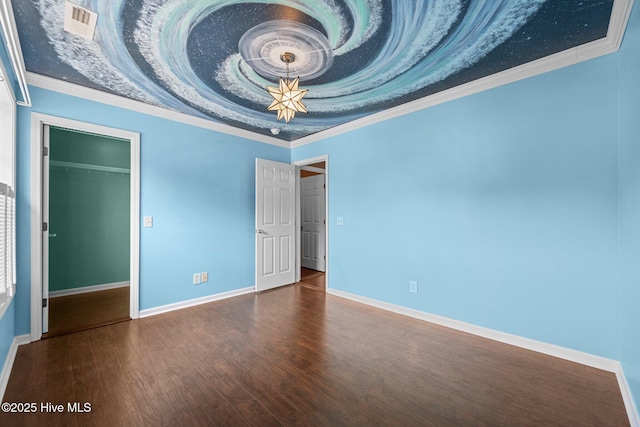 interior space featuring wood finished floors, baseboards, a raised ceiling, a spacious closet, and ornamental molding