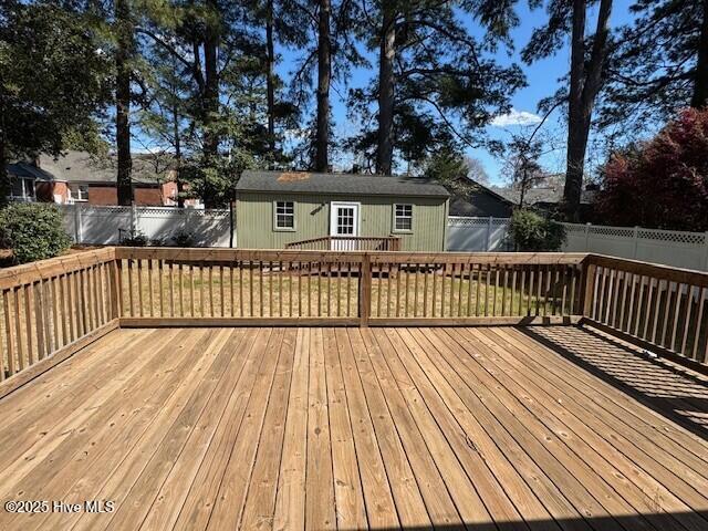 deck with a fenced backyard, a lawn, and an outbuilding