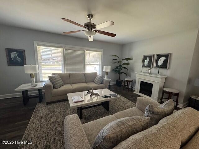 living area featuring a ceiling fan, dark wood-style floors, baseboards, and a fireplace
