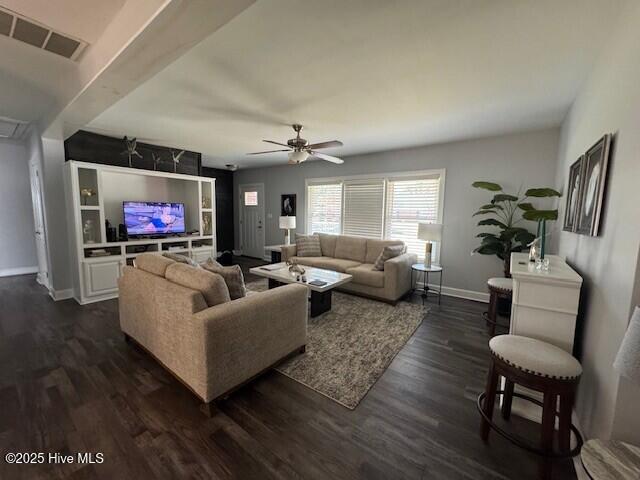 living room featuring baseboards, visible vents, a ceiling fan, and dark wood finished floors
