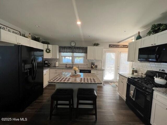 kitchen with white cabinetry, a center island, backsplash, light stone counters, and black appliances