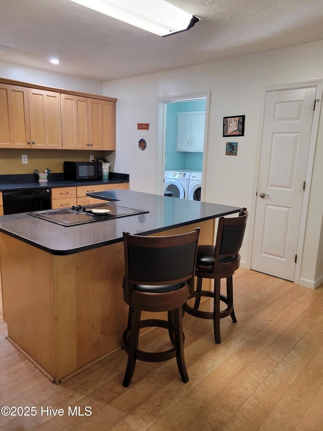 kitchen featuring washing machine and dryer, dark countertops, a center island, light wood-type flooring, and black appliances
