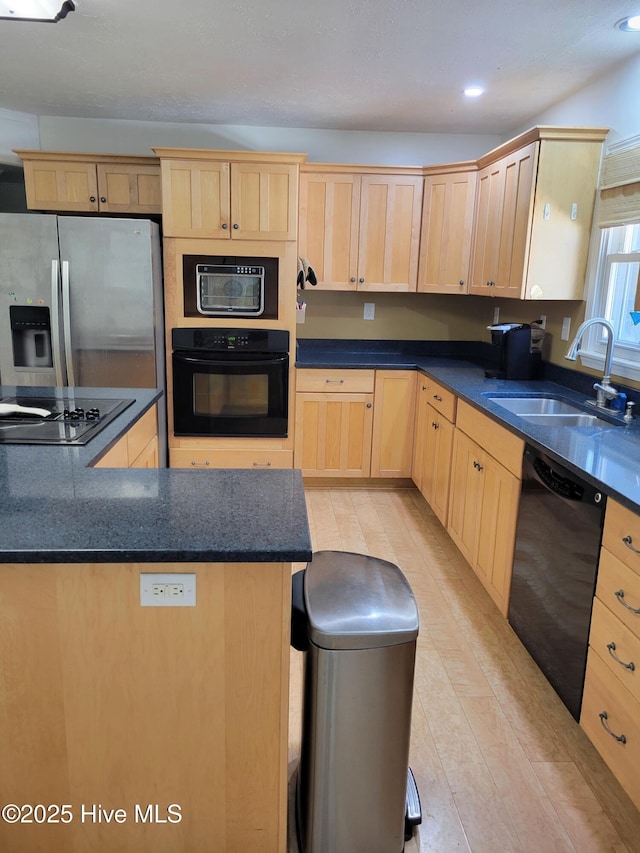 kitchen with light brown cabinetry, dark countertops, a sink, and black appliances