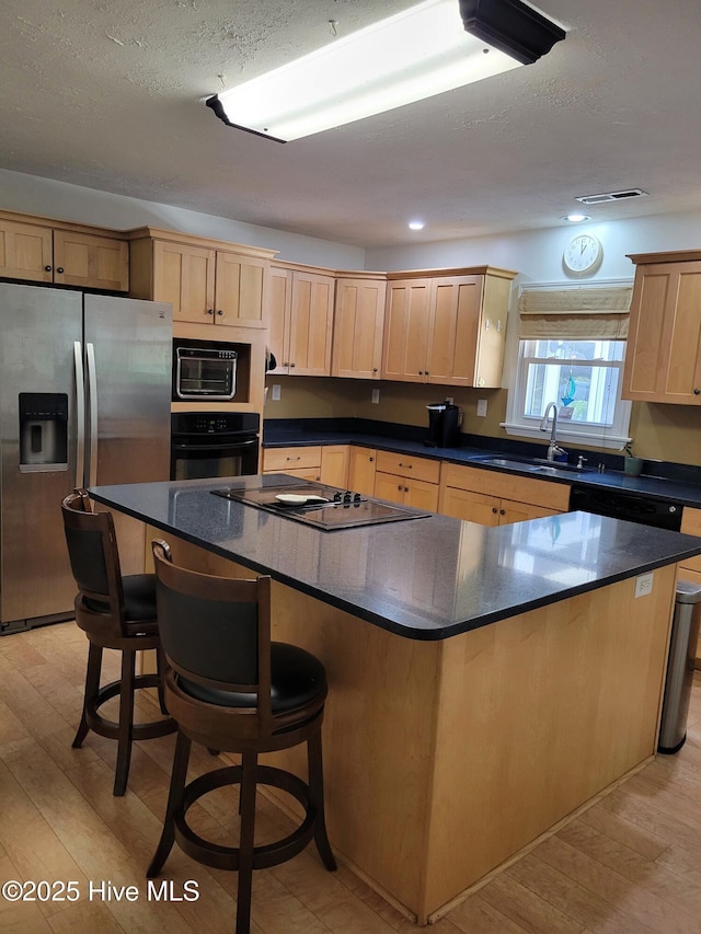 kitchen with light brown cabinets, a center island, a sink, light wood finished floors, and black appliances