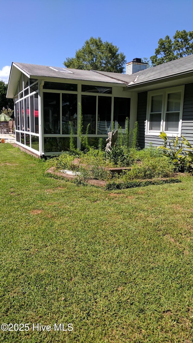back of house featuring a yard, a chimney, and a sunroom