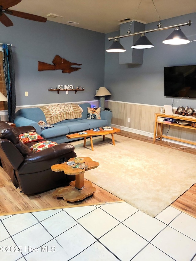 living area featuring a wainscoted wall, tile patterned flooring, ceiling fan, and visible vents