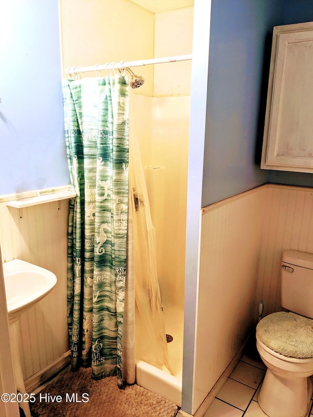 full bath with a wainscoted wall, tile patterned flooring, a shower stall, and toilet