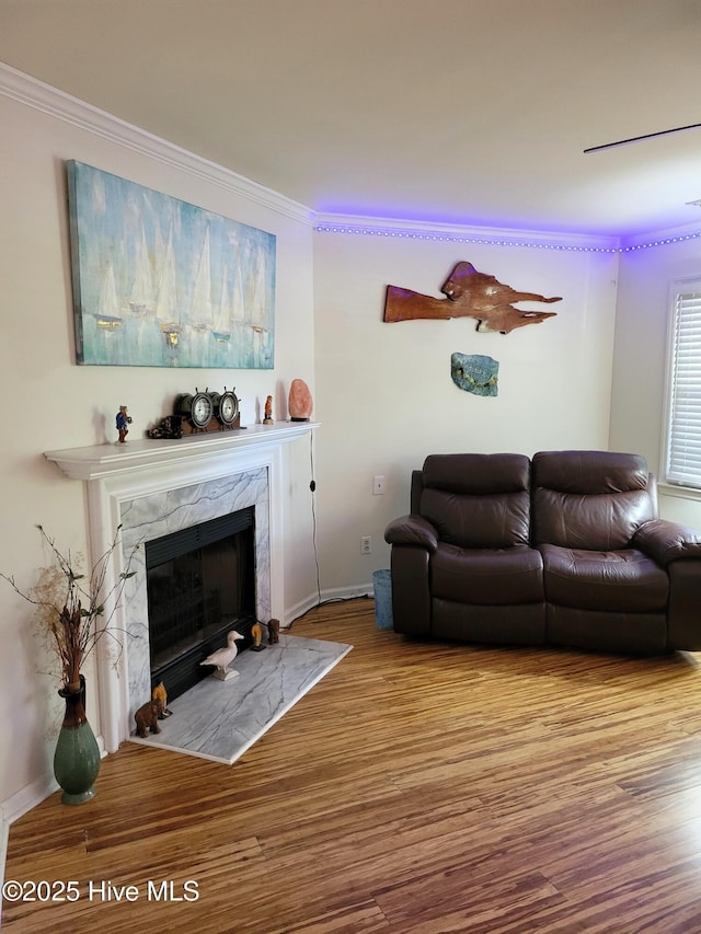 living area featuring a high end fireplace, baseboards, ornamental molding, and wood finished floors