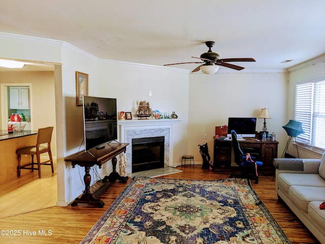 living area featuring a premium fireplace, a ceiling fan, ornamental molding, and wood finished floors