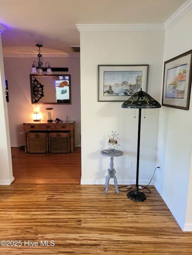 corridor with crown molding, baseboards, visible vents, and wood finished floors