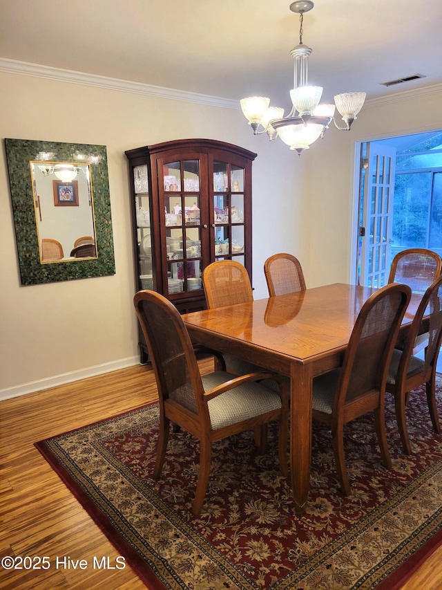 dining room featuring an inviting chandelier, ornamental molding, wood finished floors, and visible vents
