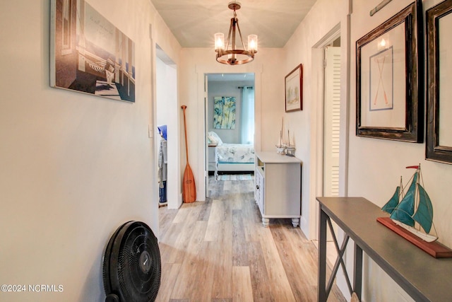 corridor with light wood finished floors and an inviting chandelier