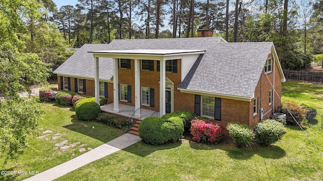 neoclassical home with a chimney, a shingled roof, a porch, brick siding, and view of scattered trees