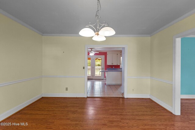 unfurnished dining area with a chandelier, ornamental molding, baseboards, wood finished floors, and a ceiling fan
