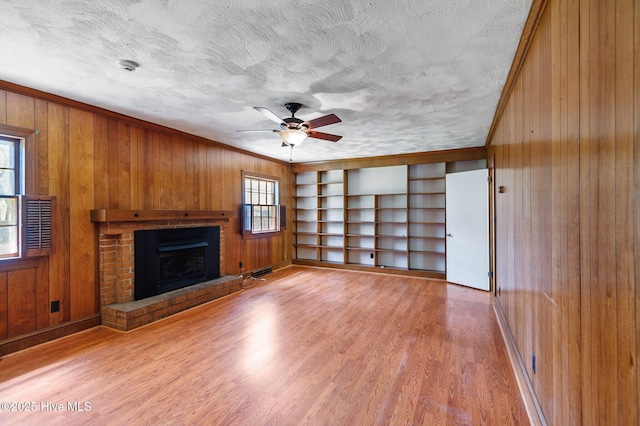 unfurnished living room featuring wooden walls, a brick fireplace, light wood-style flooring, ceiling fan, and baseboards
