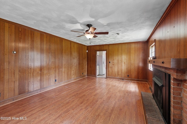 unfurnished living room featuring a brick fireplace, ceiling fan, wooden walls, light wood finished floors, and baseboards
