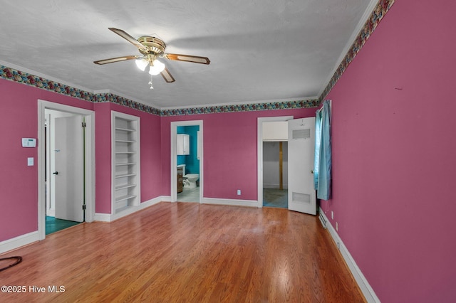 spare room with built in features, a ceiling fan, wood finished floors, baseboards, and ornamental molding