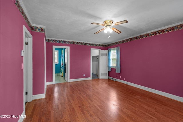 unfurnished bedroom featuring a spacious closet, wood finished floors, baseboards, crown molding, and a closet